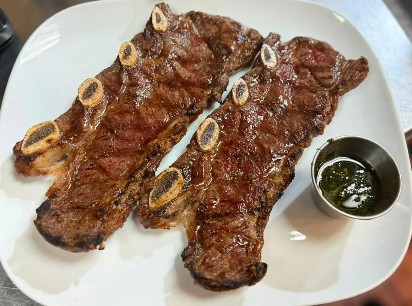 Two charcoal-grilled bone-in short ribs served with chimichurri